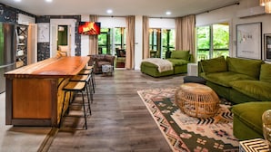 Un salon moderne avec un bar en bois, des canapés verts et un tapis à motifs.