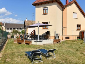 Un espace patio aménagé avec du mobilier d’extérieur, un barbecue et un grand parasol.