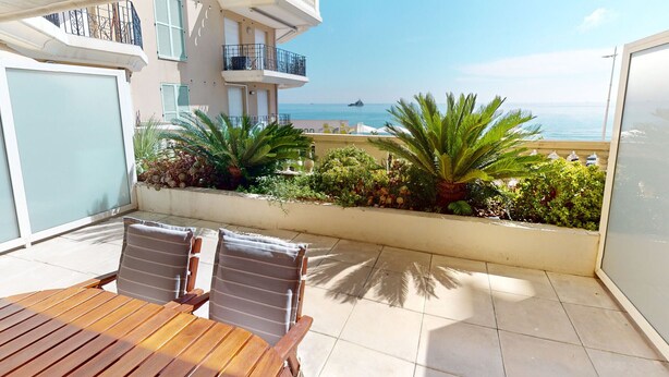 Un balcon avec une table et des chaises en bois, une vue sur la mer et quelques plantes.