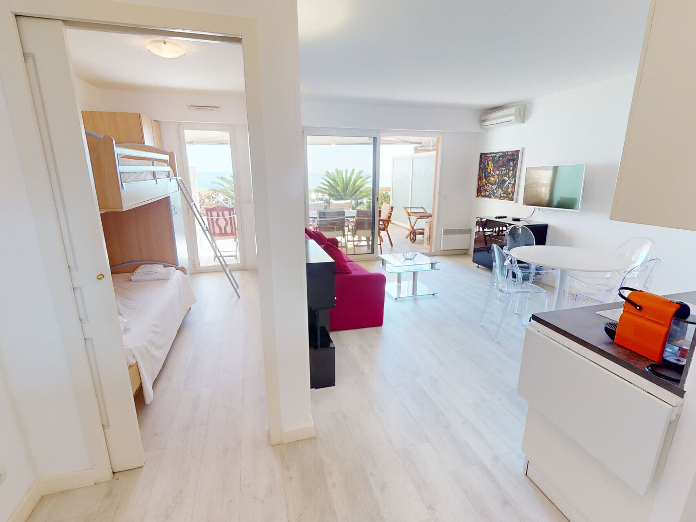 A modern, open-plan living area with a kitchen, dining area, and a balcony with outdoor furniture.