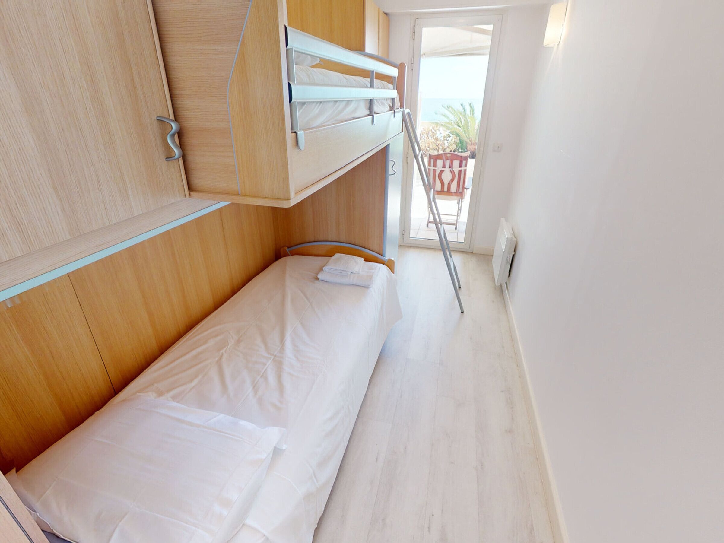 A compact room with a bunk bed, wooden wardrobe, and a door leading to a balcony.