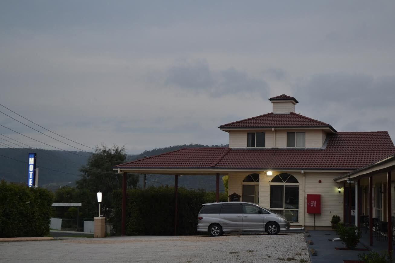 Un motel con una zona de estacionamiento techada, un edificio de una sola planta y un coche aparcado al frente.