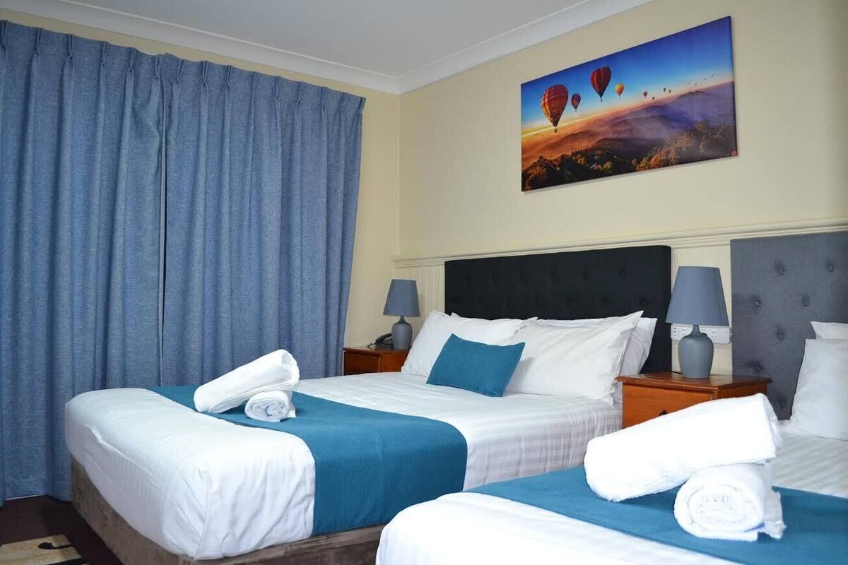 Habitación de hotel con dos camas, un cuadro grande de globos aerostáticos y vista al cielo.