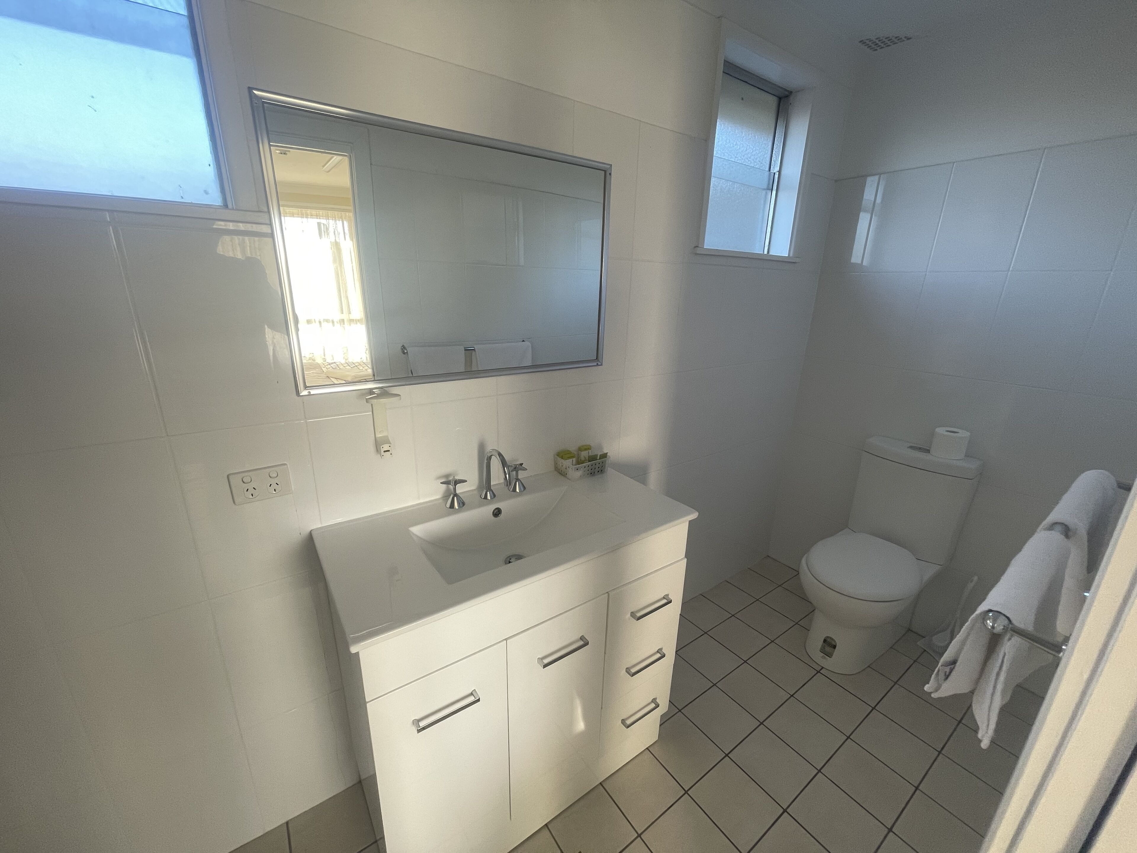 Baño con lavamanos, espejo y retrete blancos.