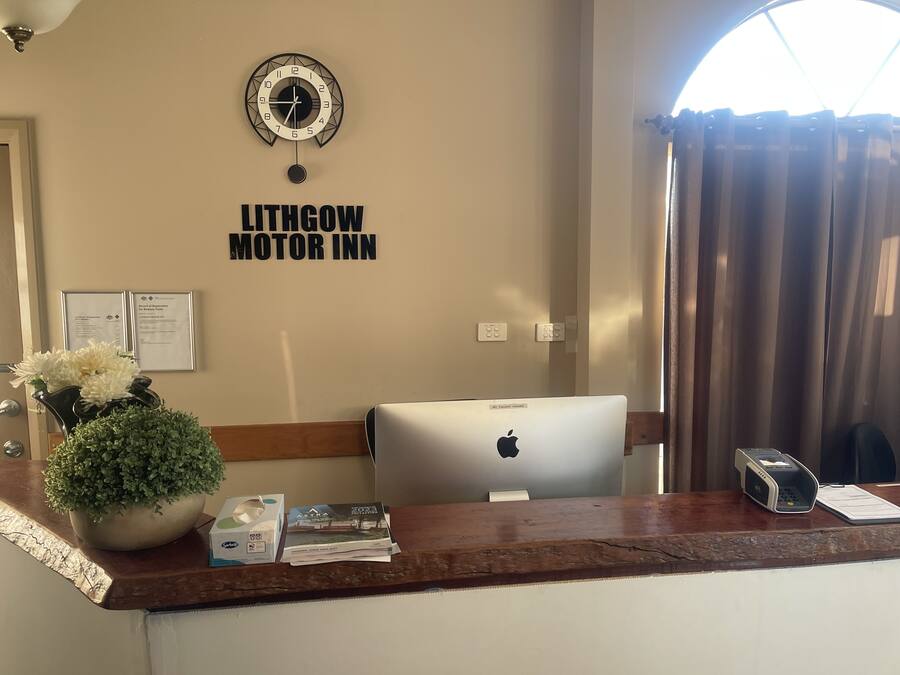 A reception desk at Litgow Motor Inn with a clock, framed certificates, a potted plant, and a laptop.