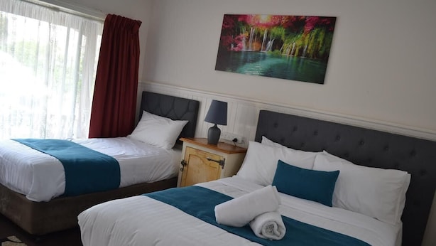 Habitación de hotel con dos camas, cada una con ropa de cama blanca y detalles en color verde azulado, una mesita de noche de madera con una lámpara y un cuadro de una cascada en la pared.