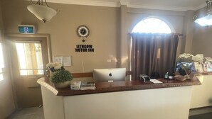 Una recepción con una computadora portátil, un reloj y un letrero que dice "Lithgow Motor Inn".