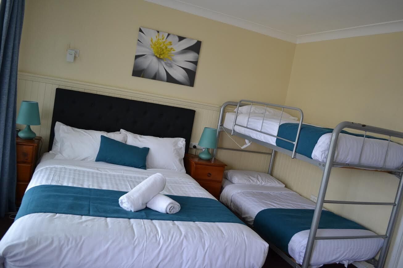 A hotel room with a large bed, a smaller bed, and a bunk bed. There are two bedside tables with lamps.