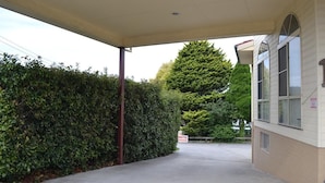 Un paseo techado conduce a un edificio con un letrero que dice 'Motel', rodeado de abundante follaje y un gran árbol de hoja perenne.