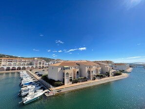 A marina with boats docked, a building with arches, and a bridge in the background.