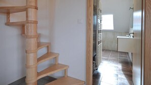 A wooden spiral staircase leading to a bathroom with a modern sink and a radiator. - Bright and quiet cottage with terrace, barbecue, and parking 5 km from Colmar (Houssen)