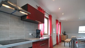 A modern kitchen with a built-in oven, a coffee maker, and red curtains. - Bright and quiet cottage with terrace, barbecue, and parking 5 km from Colmar (Houssen)