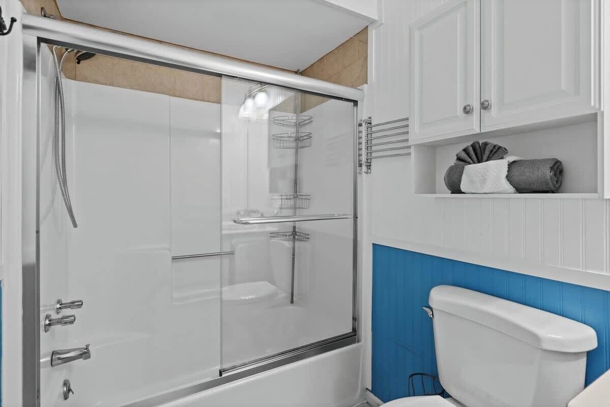 Een badkamer met een douche met glazen wand, een wit toilet en een blauwe accentmuur.