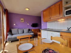 Um espaço compacto com cozinha compacta, sofá, mesa de jantar para dois e televisão na parede.