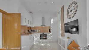 Eine moderne Küche mit weißen Schränken, einem eingebauten Backofen, einer Mikrowelle und einem großen Fernseher an der Wand.