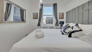 Ein Hotelzimmer mit einem großen Bett, einem fensterbelaubten Fenster, einem Kopfteil und zwei an der Wand hängenden Bildern.