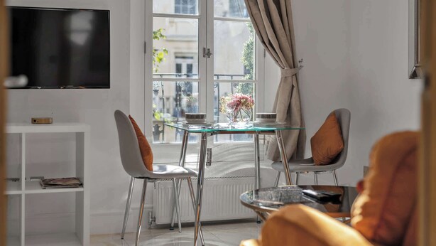 Ein modernes Wohnzimmer mit einem Glastisch, zwei Stühlen, einem Fernseher und Blick auf die Straße.