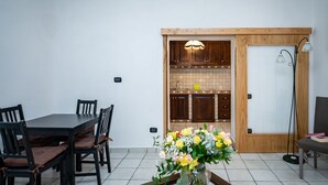 Een eethoek met een houten tafel en stoelen, een bloevas en een keuken die door een open deur zichtbaar is.