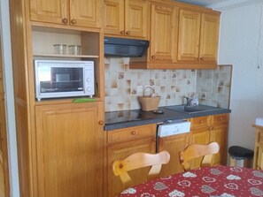 A compact kitchen with wooden cabinets, a microwave, a sink, and a dining area with a table and chairs. - Spacious central studio near gondola, sunny balcony (Châtel)