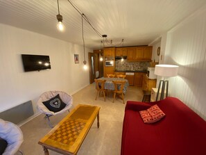 A living room with a red sofa, a wooden coffee table, a television, and a kitchen in the background.