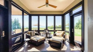 A sunroom with large windows, a ceiling fan, and outdoor seating.