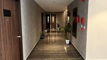 A hallway with a tiled floor, a wooden door, a potted plant, and an exit sign.