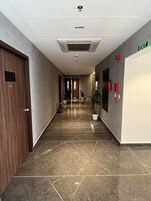Un pasillo con suelo de baldosas, una puerta de madera, una planta en maceta y una señal de salida.