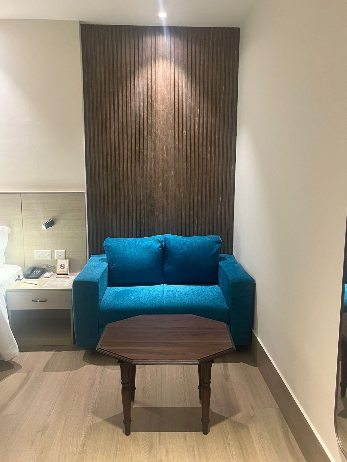 Una habitación moderna con un sofá azul, una mesa de centro de madera, una mesita de noche con un teléfono y una pared con listones de madera verticales.