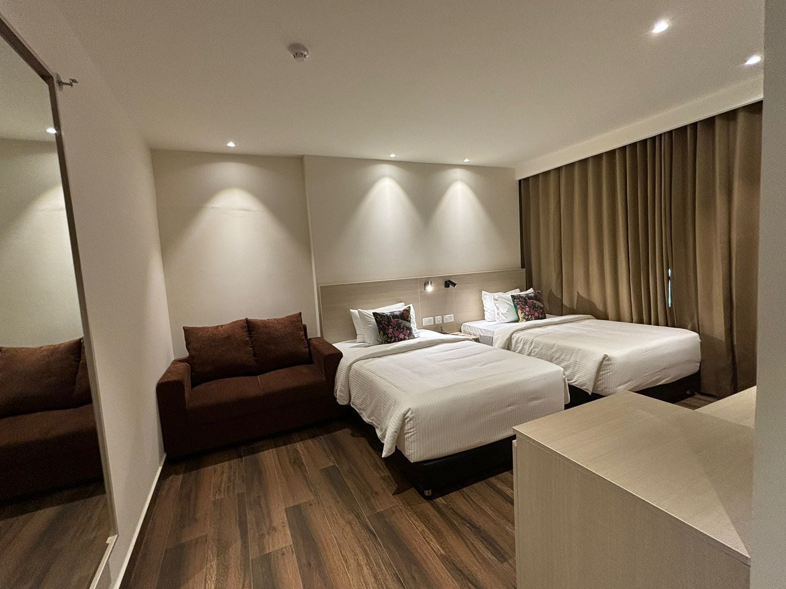 A hotel room with two beds, a sofa, and a wooden floor.