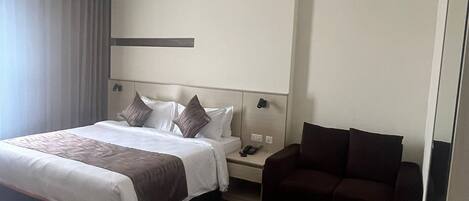Una camera d'albergo moderna con un letto grande, un divano scuro, un comodino e una ventola a soffitto.