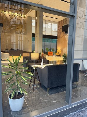 Um hall moderno com balcão de recepção, área de estar e uma grande planta em vaso.