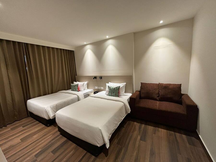A hotel room with two single beds, a brown sofa, and a wooden floor.