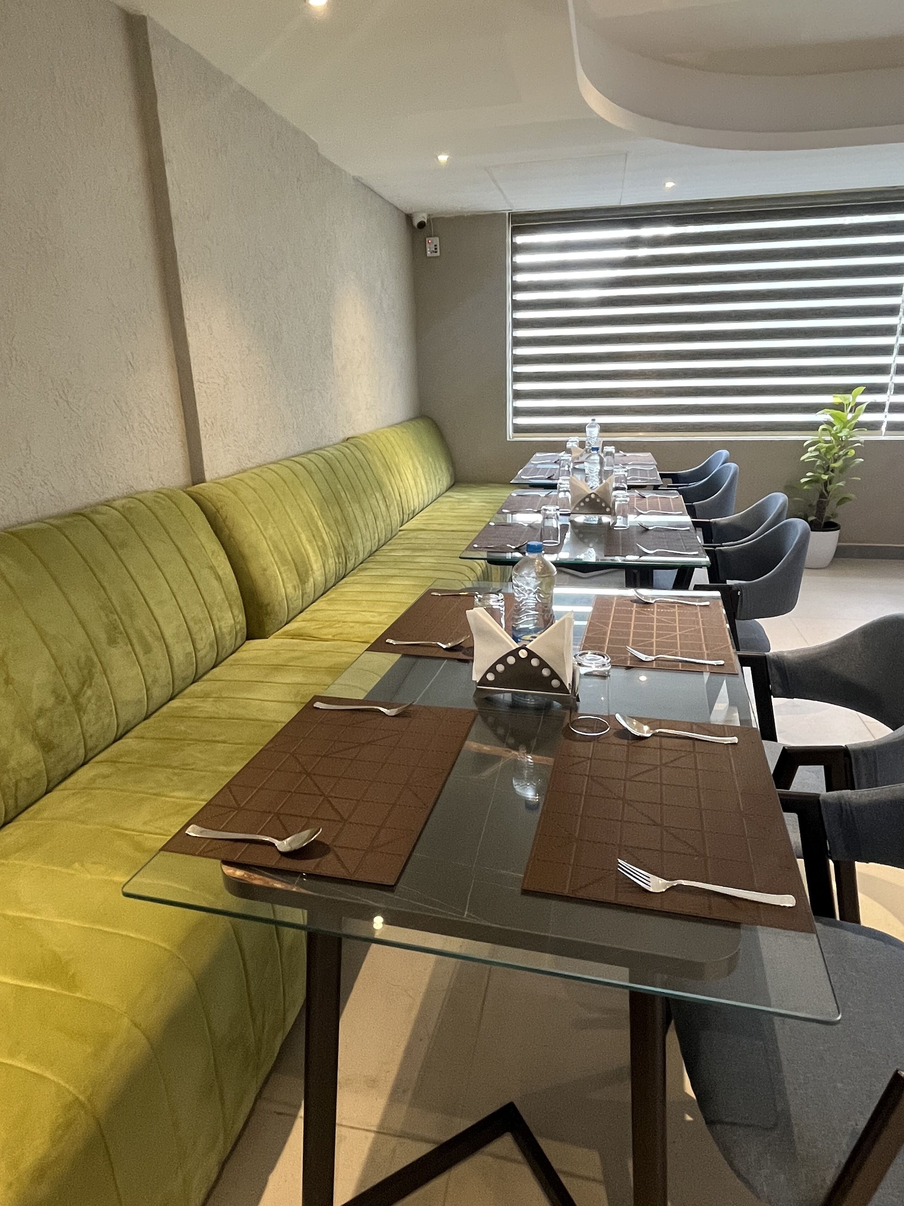 A dining area with a glass table set for six, a green sofa, and a potted plant.