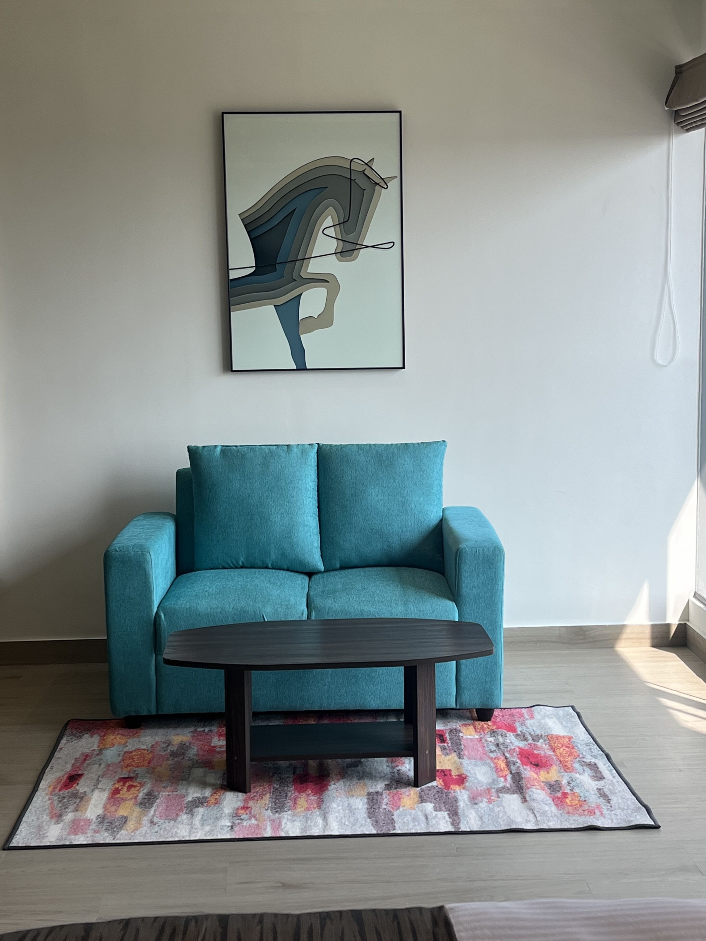 A teal sofa with a dark wooden coffee table, a colorful rug, and a framed abstract painting on the wall.