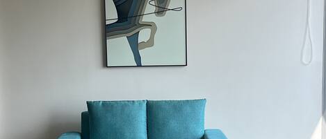 Ein türkisfarbenes Sofa mit einem dunklen Holztisch, einem bunten Teppich und einem gerahmten abstrakten Gemälde an der Wand.