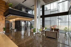 Un vestíbulo moderno con suelo de mármol pulido, una mesa de recepción, zona de estar y grandes ventanales con vistas a la ciudad.
