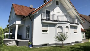 Ett tvåvåningshus med en balkong, en satellitantenn och ett litet träd på framsidan av tomten.