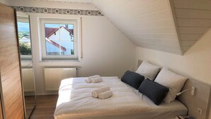 Ett sovrum med en säng, kuddar och ett fönster.