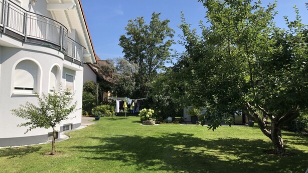 En vit byggnad med välvda fönster och en balkong, omgiven av en välskött gräsmatta och träd.