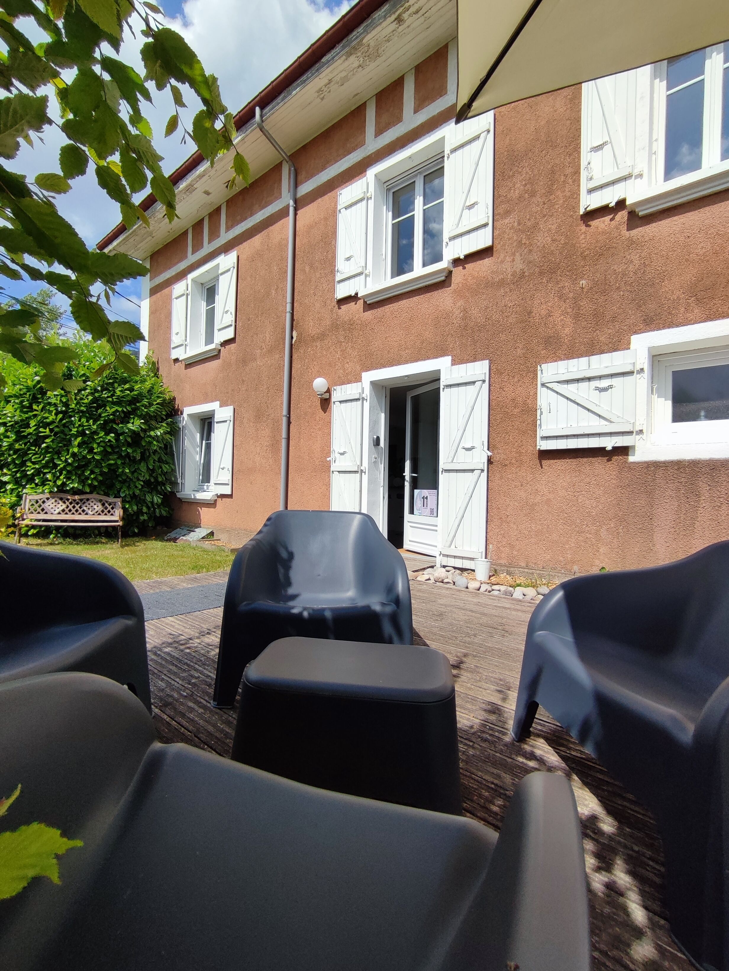 Ein Gebäude mit Backsteinfassade, weißen Fensterläden und einem überdachten Außenbereich mit Plastikstühlen.