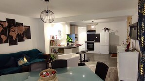 A modern living room with a glass dining table, a sofa, and a kitchen in the background.