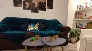 Een gezellige woonkamer met een bruine bank, een teal plaid, en een wereldkaart aan de muur. Twee kleine tafels met decoratieve items en een witte fauteuil.