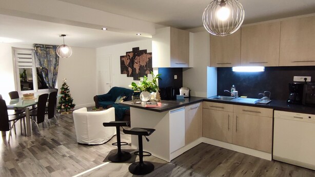 A modern kitchen with a central island, wooden flooring, and a dining area with a Christmas tree.
