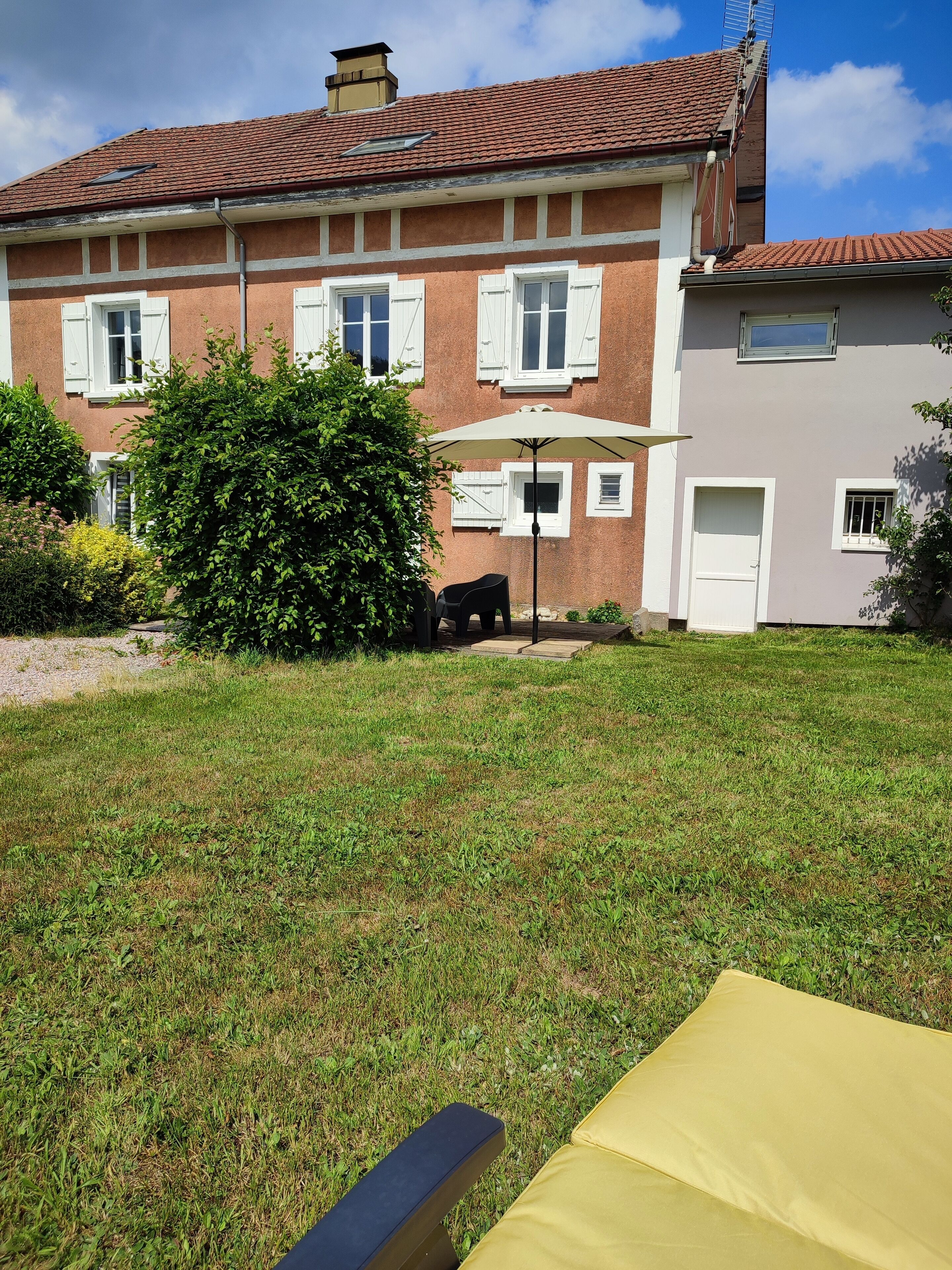 Een tweekamerhuis met een rode pannendak, een kleine tuin en een patio met een tafel en stoelen.