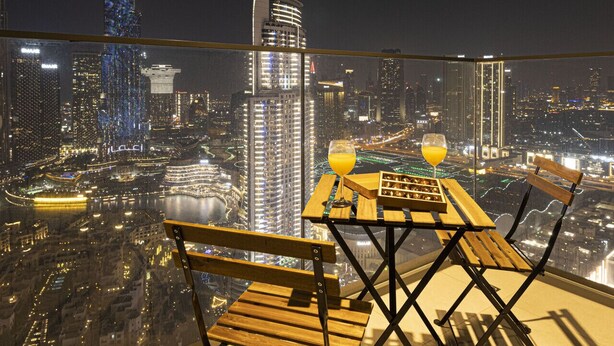 Un balcón con mesa y sillas, con vistas a un paisaje urbano iluminado de noche.