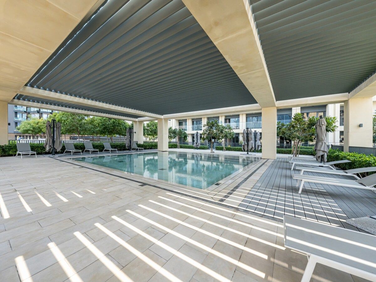 A covered outdoor swimming pool with lounge chairs and a tiled deck.
