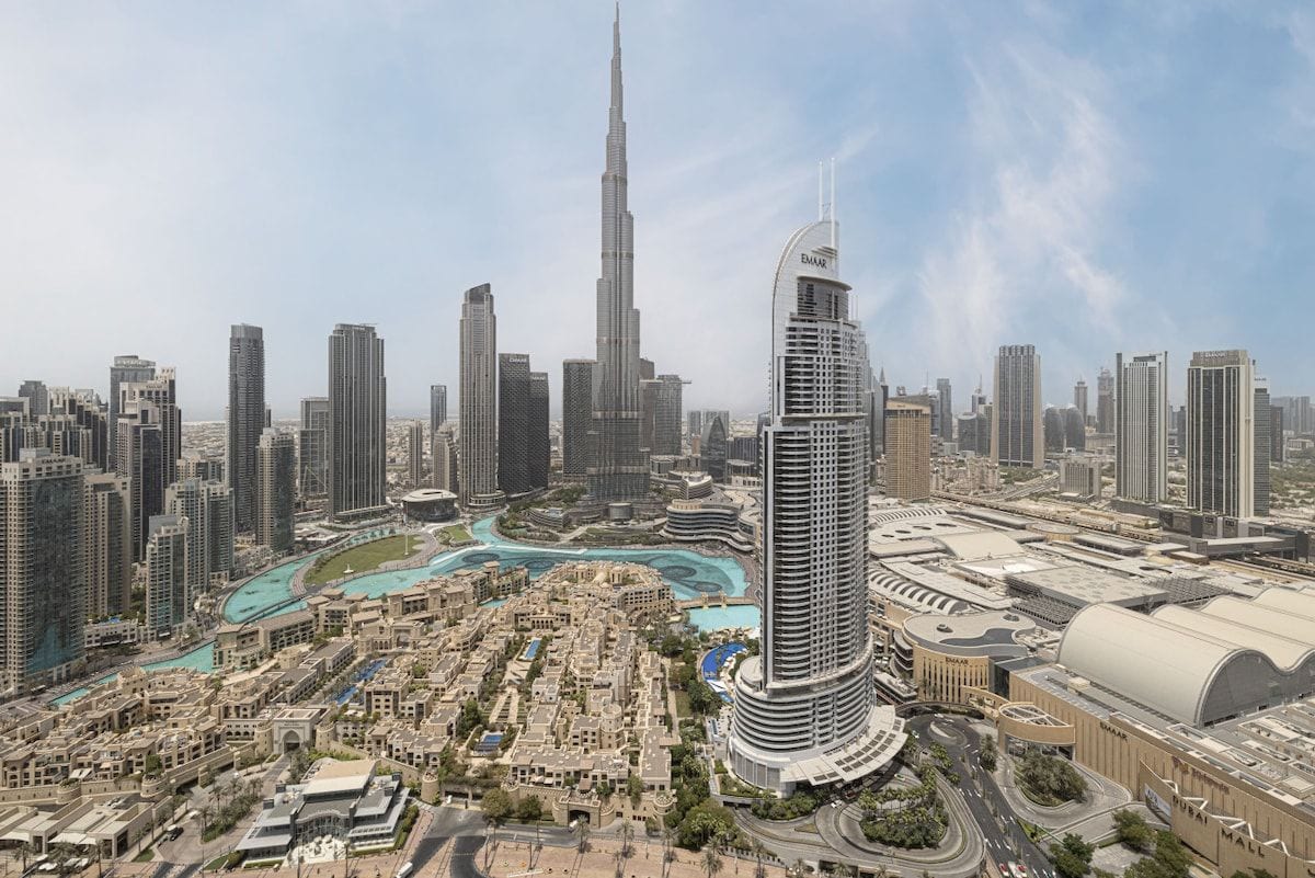 A cityscape with a prominent skyscraper, a curved building, and a dense urban area with roads and greenery.