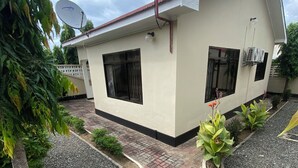 Un edificio de dos pisos con una antena parabólica, dos ventanas con rejas negras y un camino de entrada pavimentado con un área ajardinada.