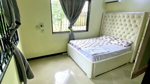 Un dormitorio con cama, ventana con cortinas, unidad de aire acondicionado y suelo de baldosas.