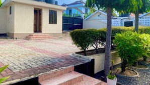 Una zona residencial con un camino pavimentado, un edificio pequeño con tanques de agua en el techo y una entrada con portón.